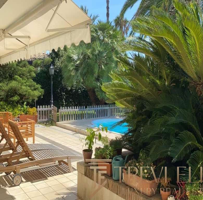 Luxurious outdoor terrace with sun loungers, lush tropical greenery, a small pool, and a white fountain fence, perfect for relaxing in a high-end Italian estate.