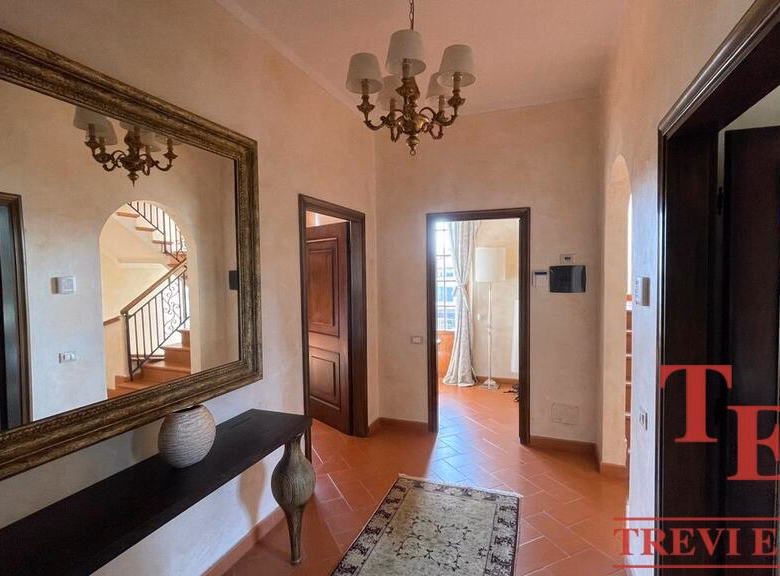Elegant hallway with mirror, chandelier, and staircase view.