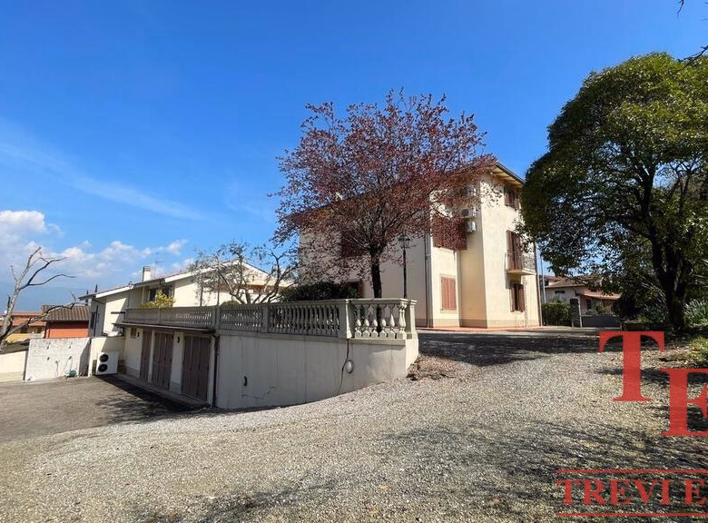 Sunny villa with driveway and lush green trees.