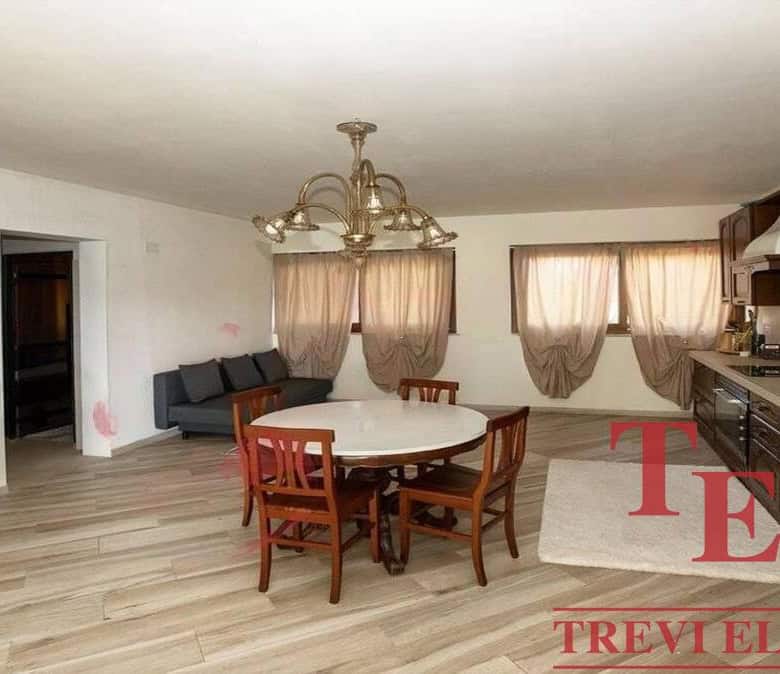 Spacious living area with wooden flooring, a round dining table, and large windows with beige curtains offering natural light in an elegant Italian home.