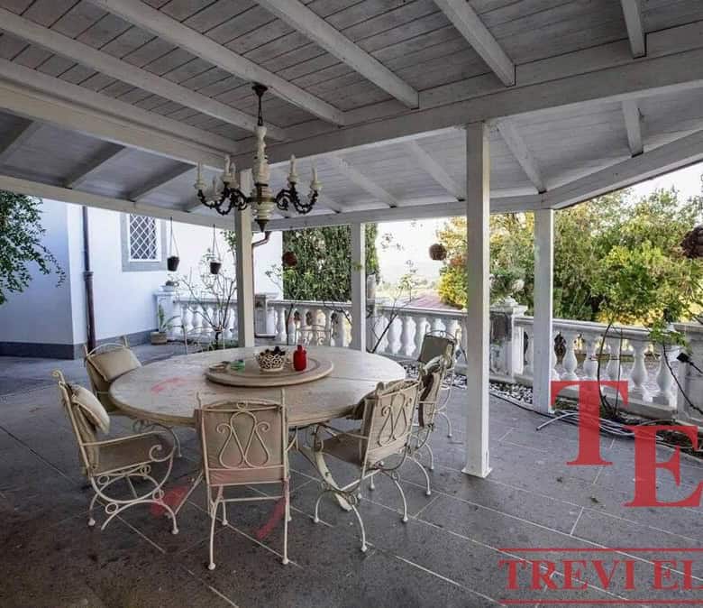 Vintage outdoor dining area on spacious covered terrace with elegant white wrought iron furniture and lush greenery, perfect for relaxing and entertaining.