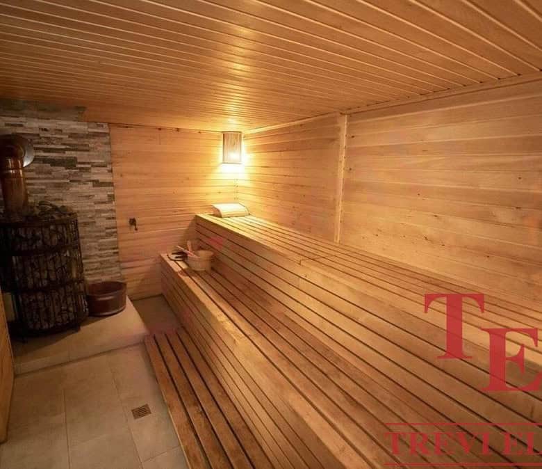 Luxurious wooden interior of a traditional sauna with warm lighting and bamboo seating, showcasing premium Italian real estate properties by Trevi Elite.
