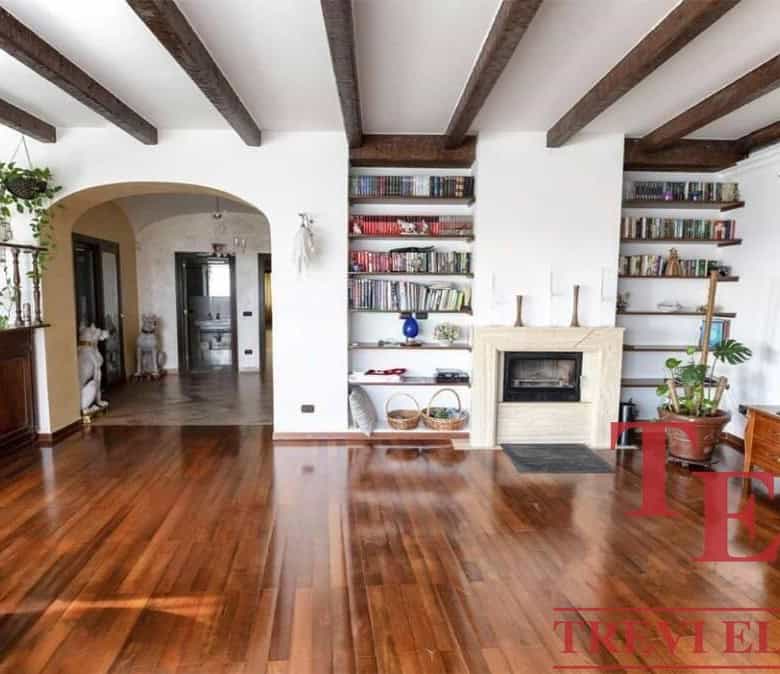 Spacious Italian living room with wooden beams, built-in bookshelves, modern fireplace, and elegant decor, showcasing luxurious real estate in Italy's prime locations.