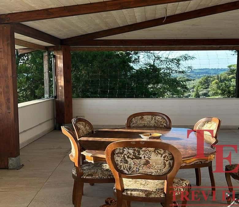Elegant Italian balcony with wooden beams and ornate dining furniture, offering panoramic views of lush greenery and rolling hills in Italy.