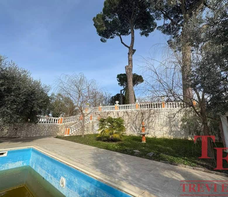 Lush backyard with a swimming pool, mature trees, and a decorative stone wall, offering a private outdoor Mediterranean oasis set in a scenic Italian landscape.