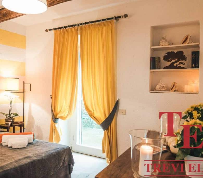 Cozy Italian bedroom with warm yellow curtains, decorative shelves, and elegant furnishings, offering a luxurious and comfortable living space in Italy's prime real estate.