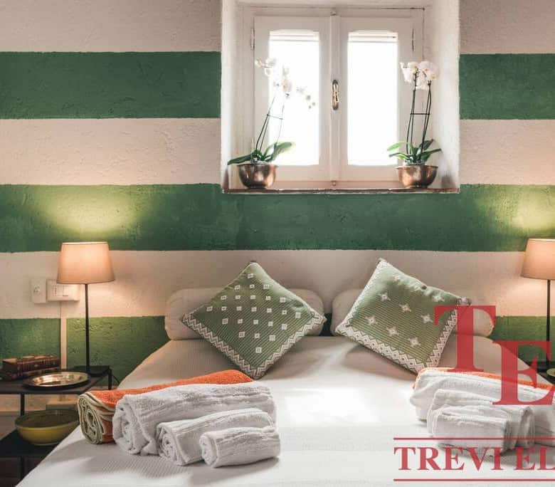 Ornate bedroom interior with striped green and white walls, modern lamps, and fresh flowers on the window sill, showcasing an inviting and stylish Italian home design.