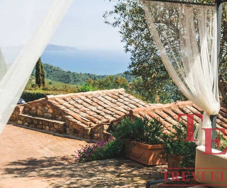 Panoramic view of Italian countryside with terracotta rooftops, lush greenery, and distant sea horizon, showcasing luxurious real estate and scenic beauty in Italy.