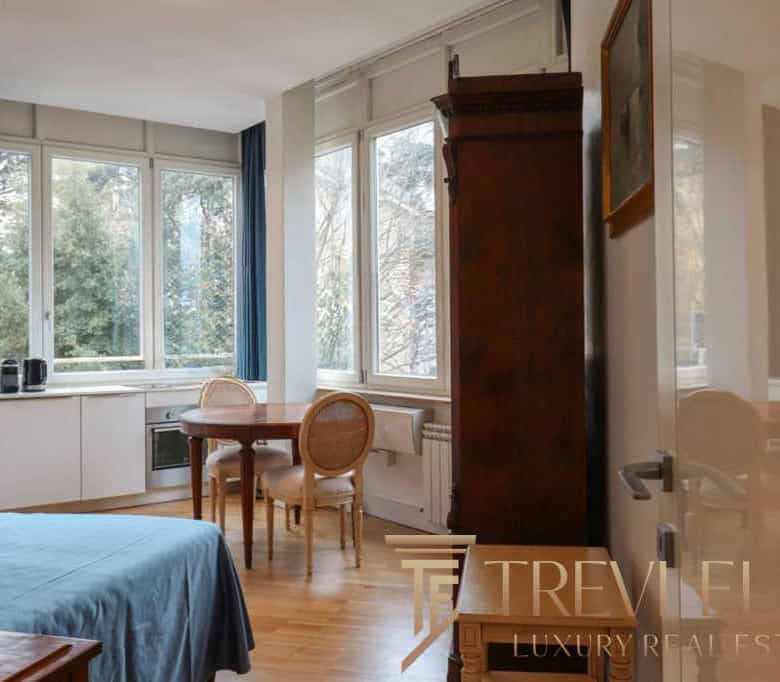 Bright and spacious living area in a luxurious Italian apartment with large windows overlooking lush greenery. Elegant furnishings and modern amenities create a comfortable atmosphere.