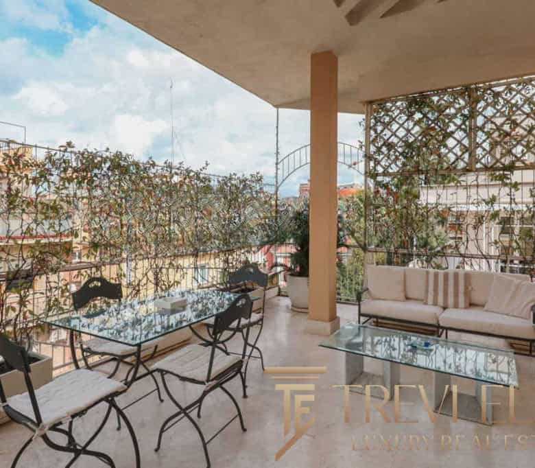 Spacious balcony with glass dining table, chairs, and cozy sofa, featuring lush greenery and the cityscape of Italy in the background.