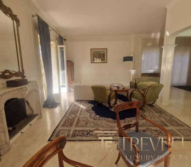 Elegant living room with antique furniture, a marble fireplace, and classic decor in a luxurious Italian estate. The space features a textured rug, framed artwork, and natural light from French doors.