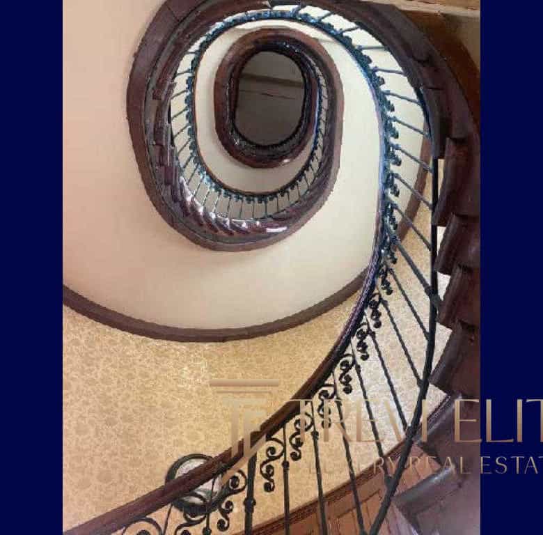 Elegant spiral staircase with ornate wrought iron railing and polished wooden handrail, showcasing luxurious Italian architecture and craftsmanship.