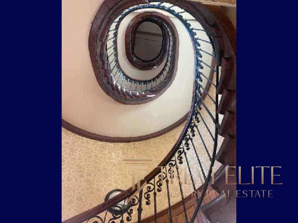Elegant spiral staircase with ornate wrought iron railing and polished wooden handrail, showcasing luxurious Italian architecture and craftsmanship.