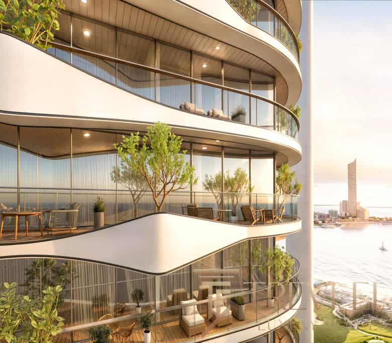 Luxurious modern residential building with curved glass balconies featuring outdoor furniture, lush greenery, and panoramic city views at sunset.
