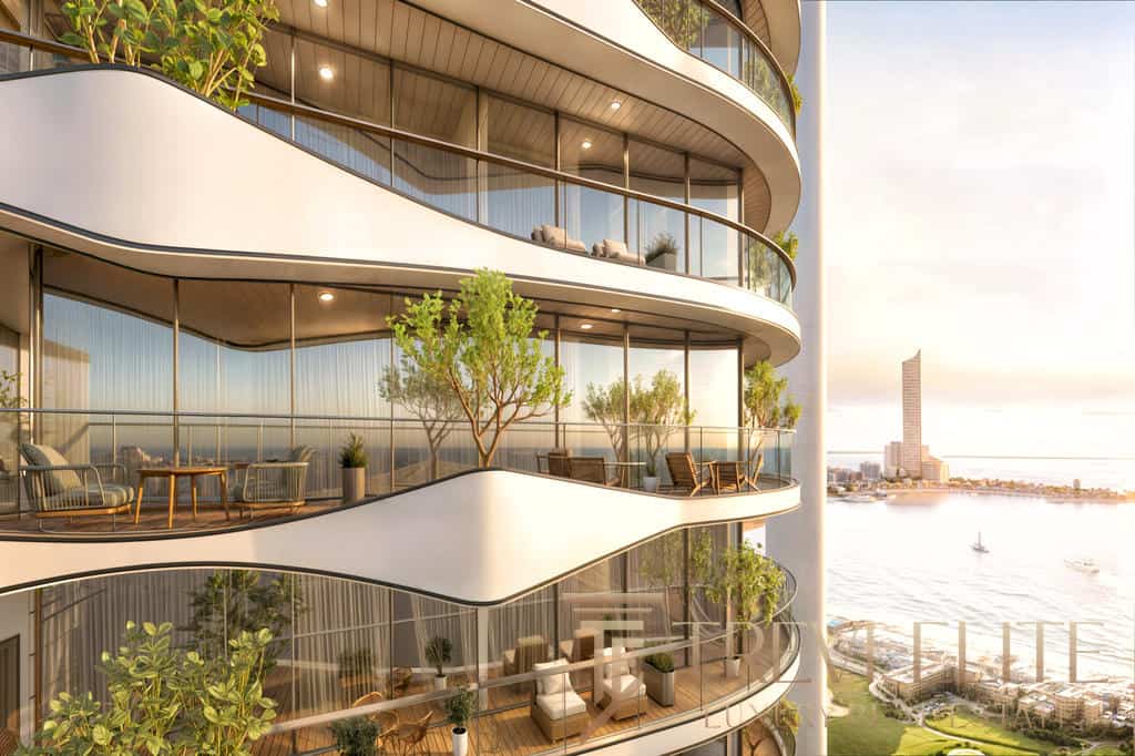 Luxurious modern residential building with curved glass balconies featuring outdoor furniture, lush greenery, and panoramic city views at sunset.