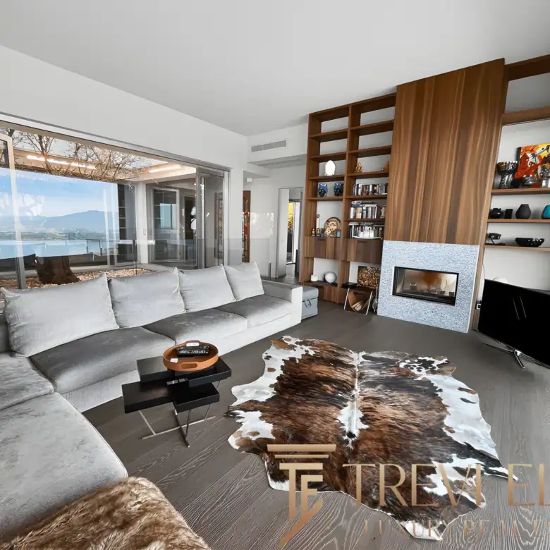 Open-plan living room with floor-to-ceiling glass, grey sofas, and panoramic Lake Maggiore views.