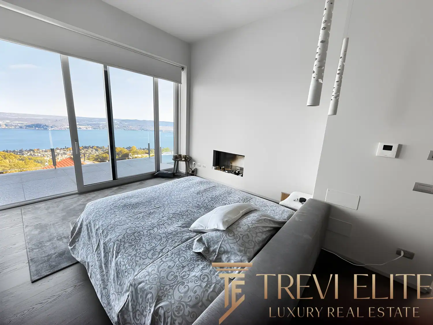 Modern bedroom with grey bedding and large sliding glass doors to the balcony.